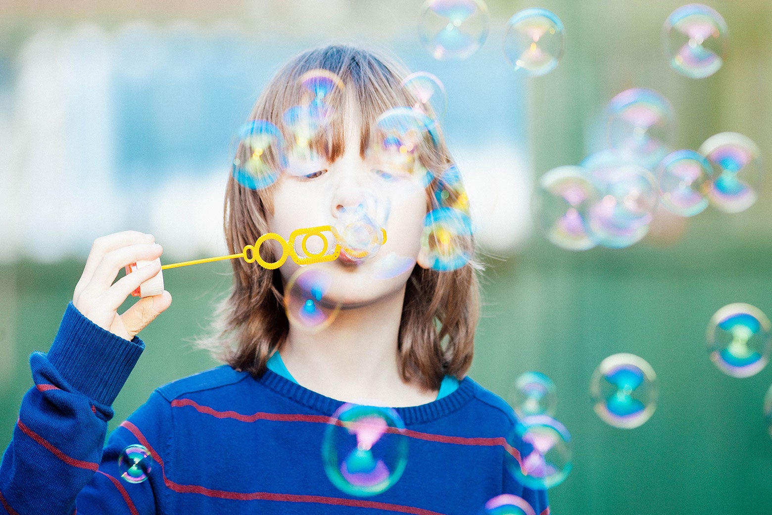 A child with long hair blows bubbles.
