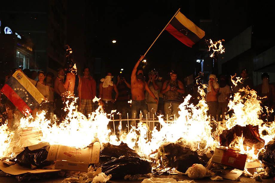 Opposition demonstrators hold a Venezuelan flag in front of a burning barricade during a protest against President Nicolas Maduro's government in Caracas.
