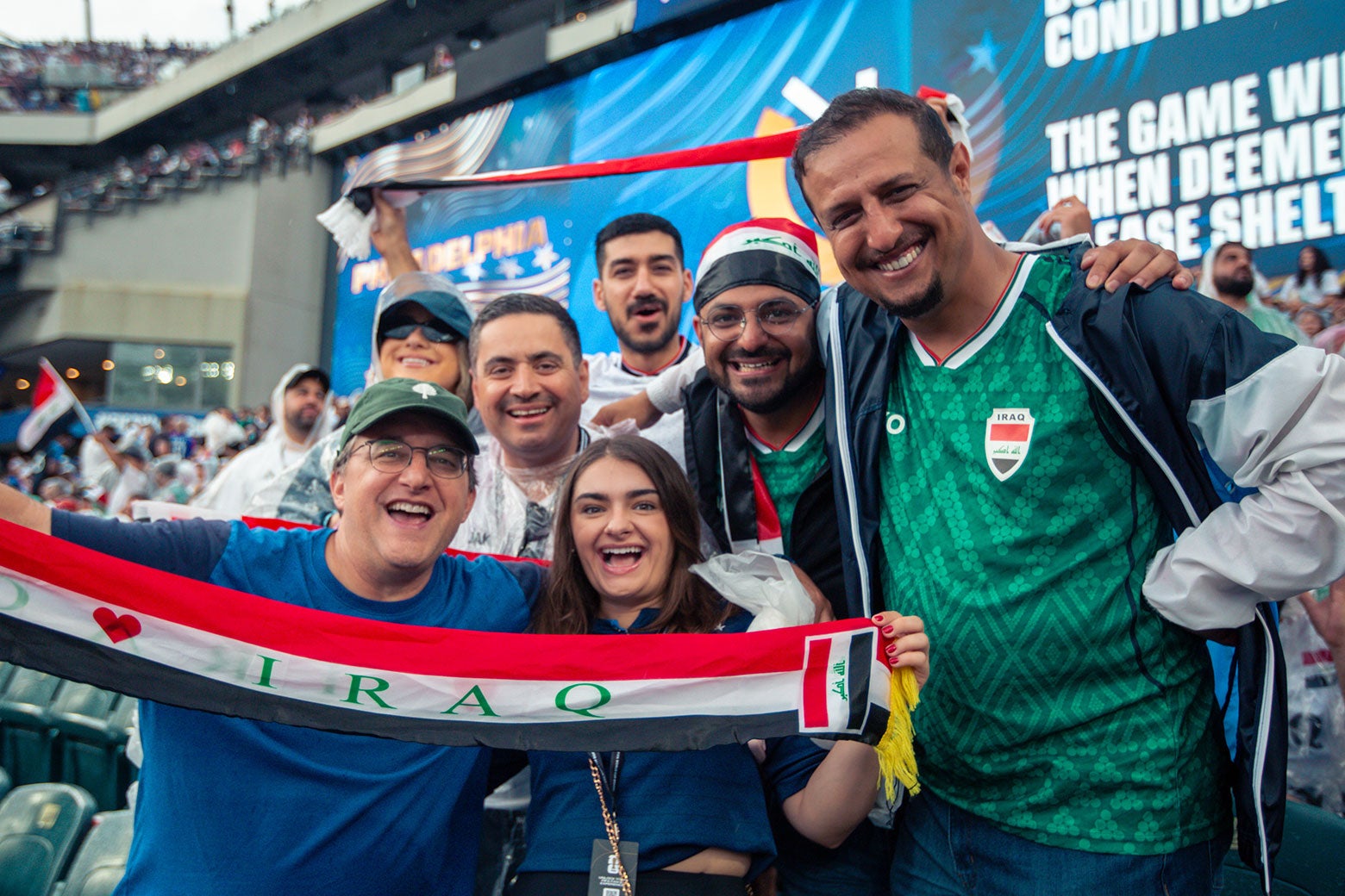 A group at the game poses smiling and holding an Iraq banner.
