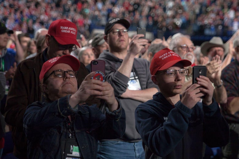 A crowd of people, many wearing MAGA hats, holding their phones up.