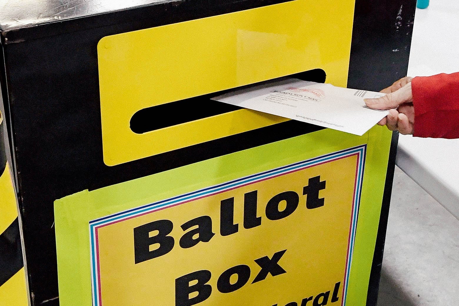 A hand puts an envelope in a box that says Ballot Box.