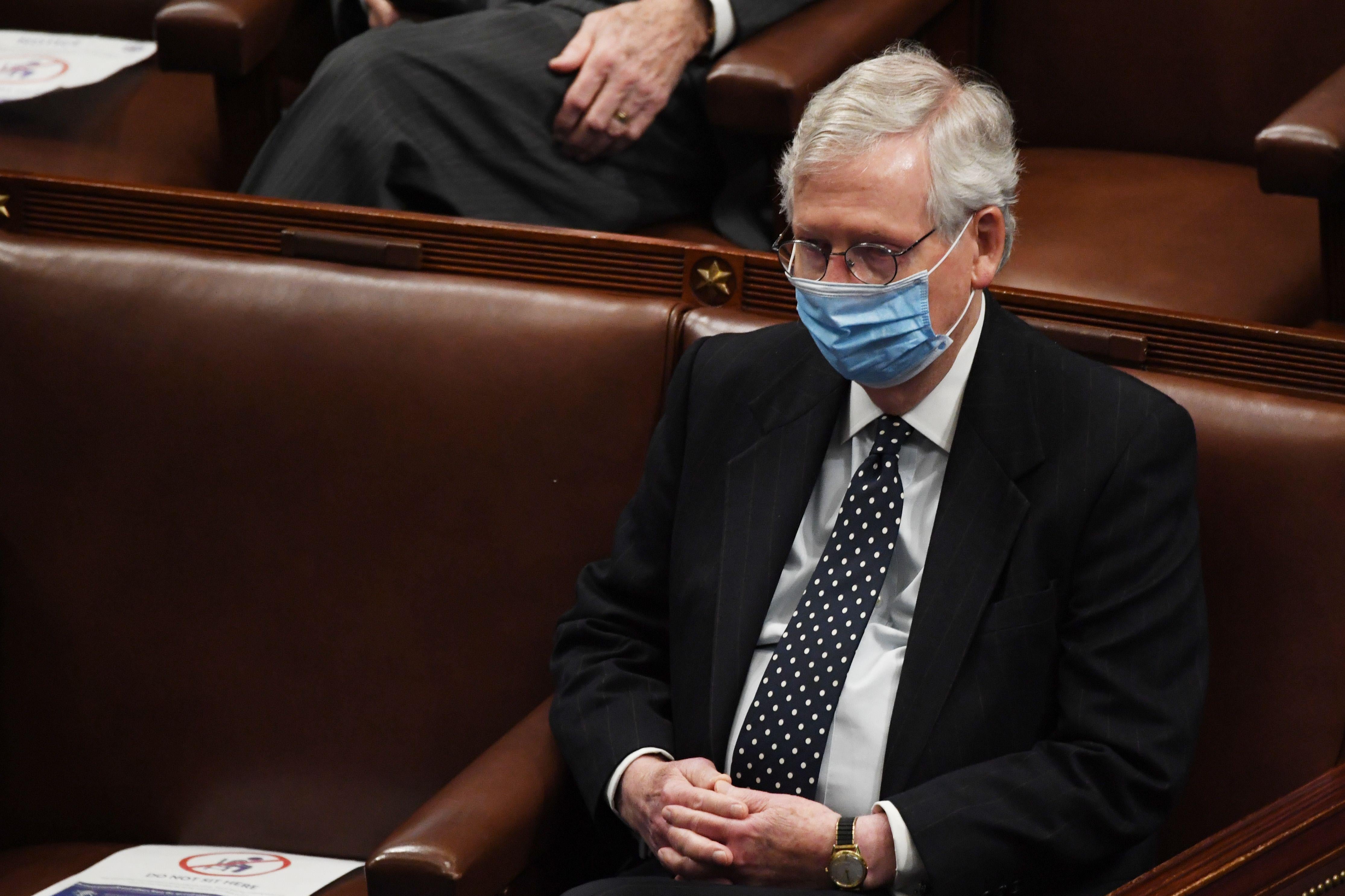 Mitch McConnell, wearing a mask, sits with his hands folded in his lap