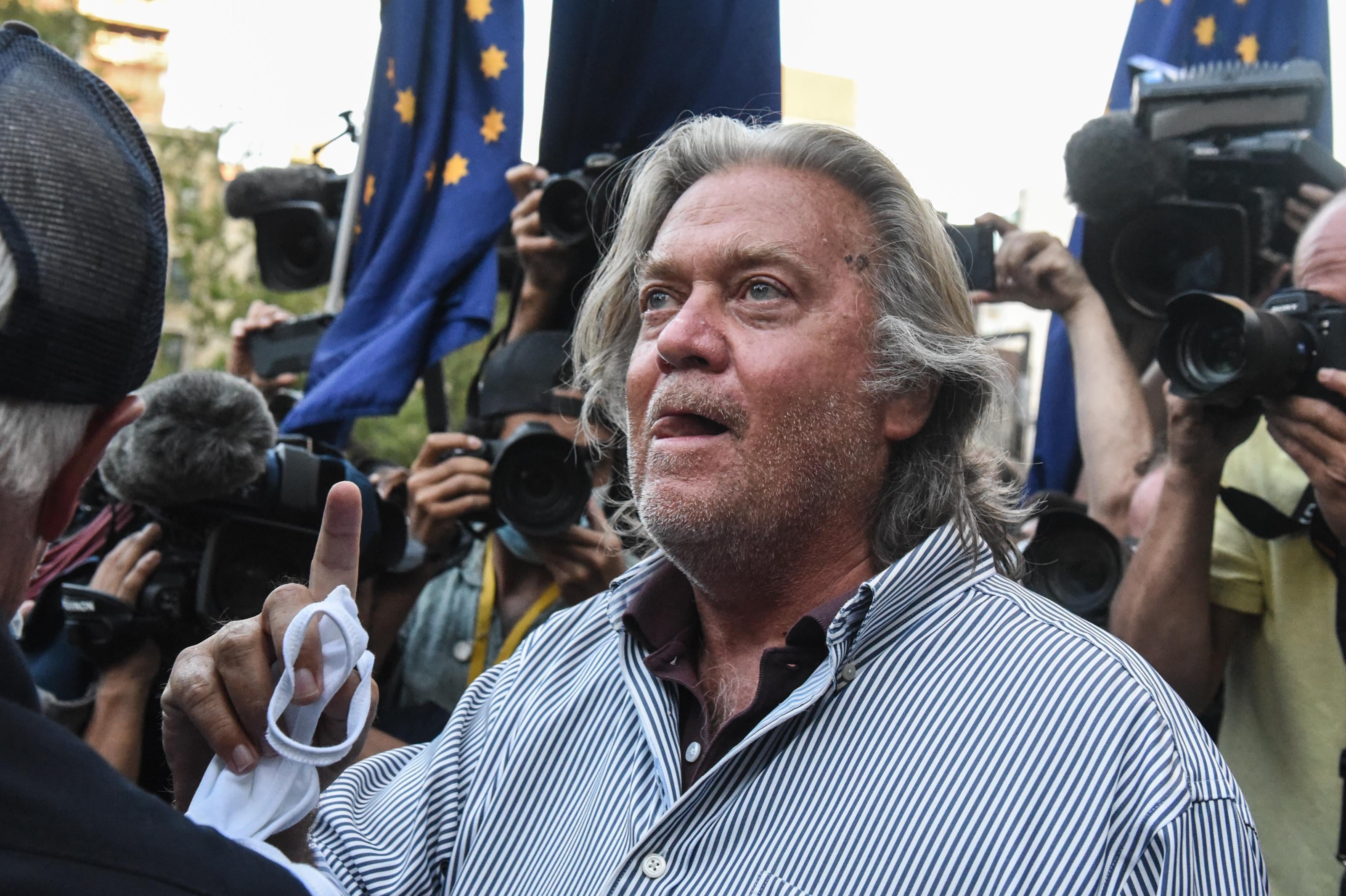 Bannon stands outside looking up and licking his lips with photographers surrounding him