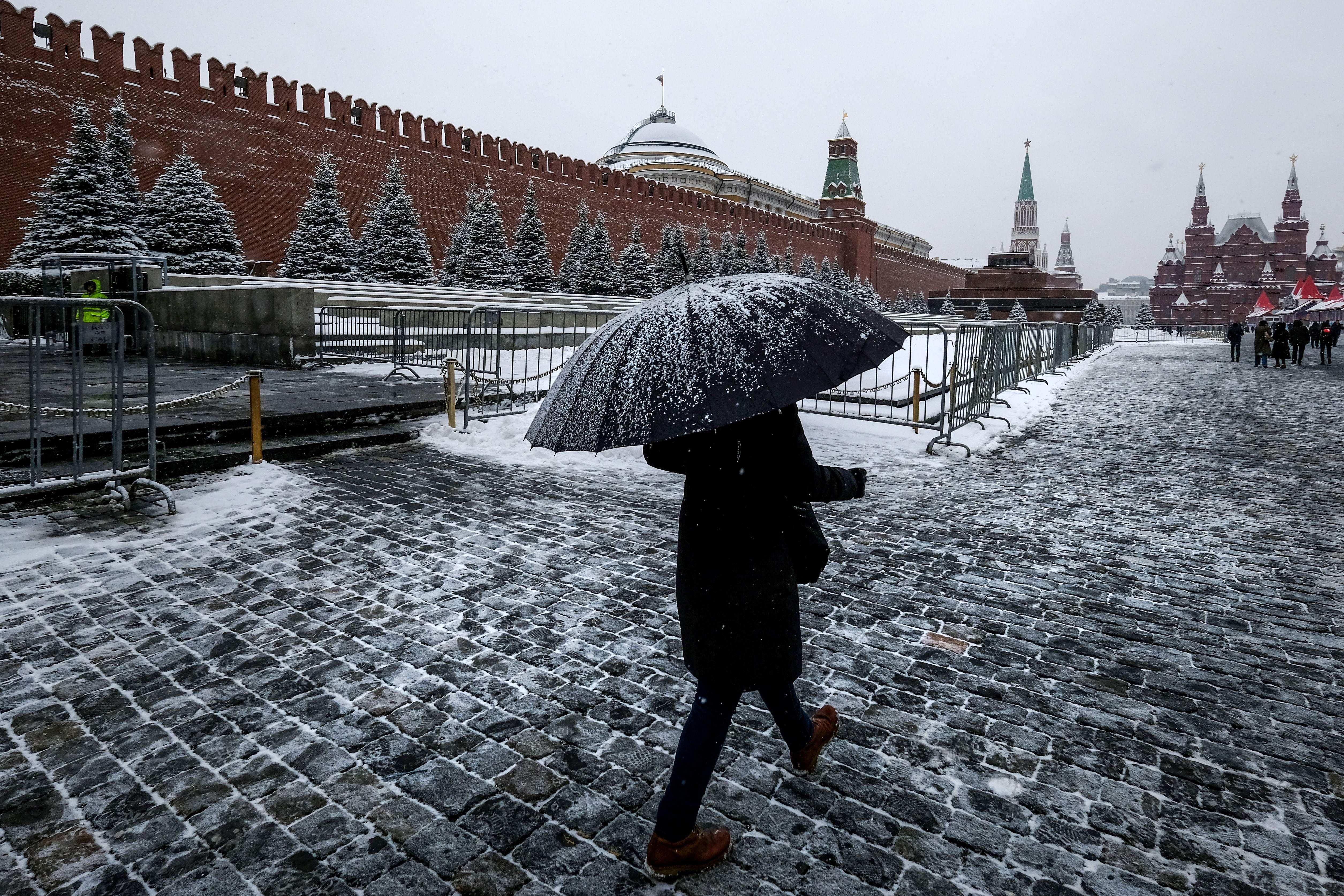 A woman with an umbrella walks on Red Square past the Kremlin after a night of heavy snowfall.