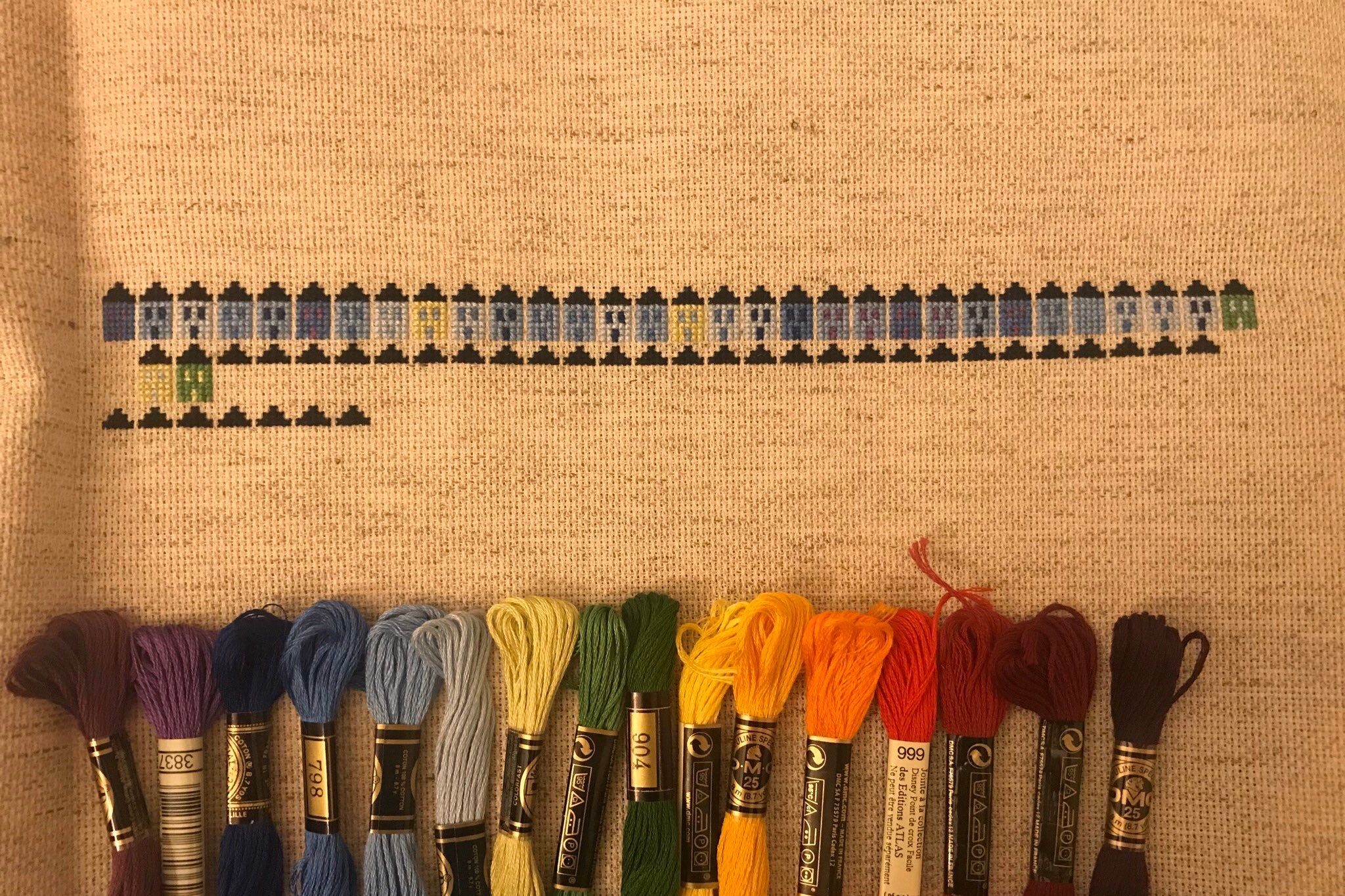 A row of cross-stitched houses in different colors, above a row of embroidery floss