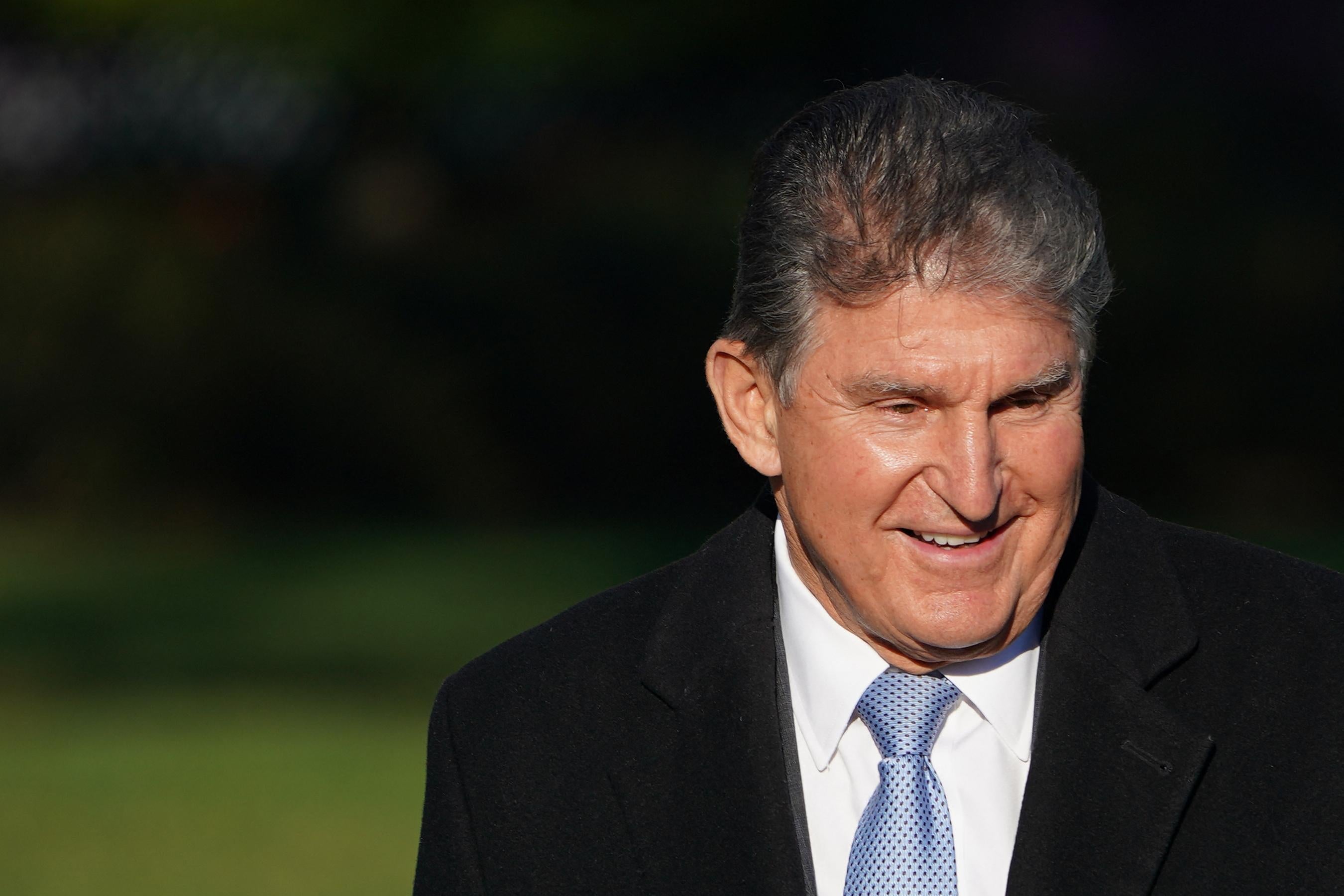 A close-up of Manchin smiling outside in a black coat and blue tie
