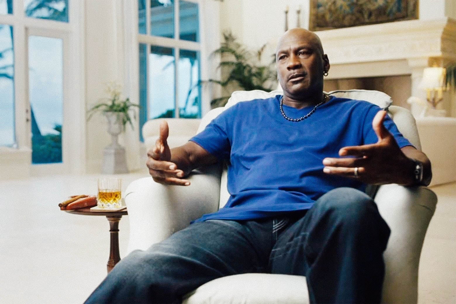 Michael Jordan sits in a chair and gesticulates.