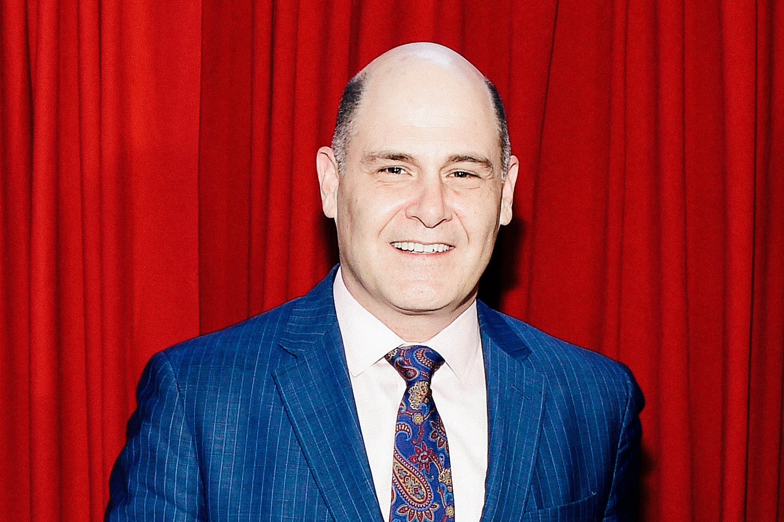 Matthew Weiner poses in front of a red curtain.