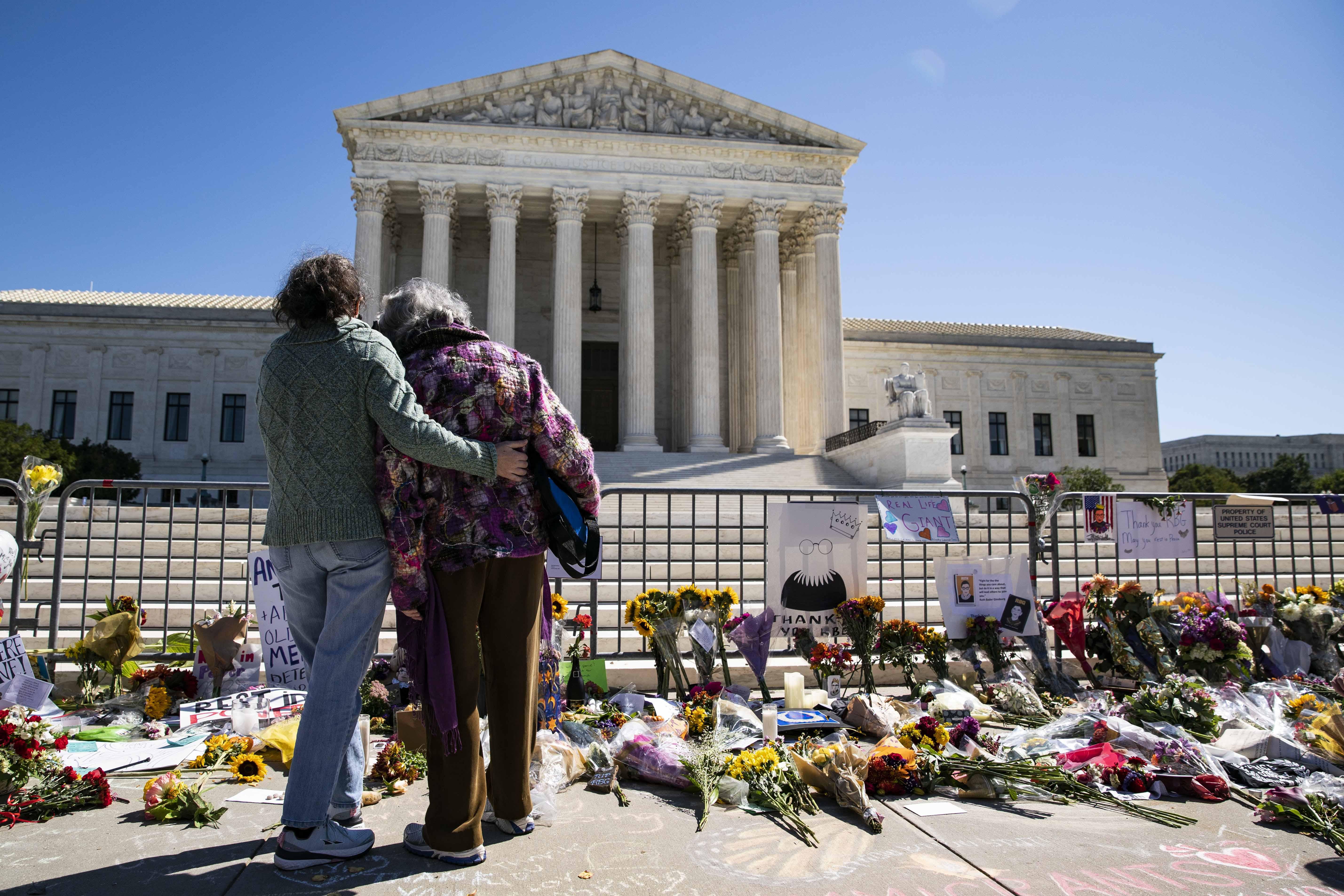 Women embrace in front of a makeshift memorial of flowers for late Supreme Court Justice Ruth Bader Ginsburg
