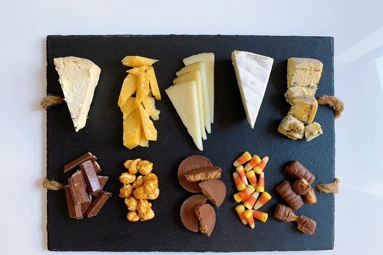 Pairs of blue cheese and Twix, brie and candy corn, manchego and Reese's, Gouda and caramel popcorn, and triple-cream cheese and Kit Kats, arranged on a serving board