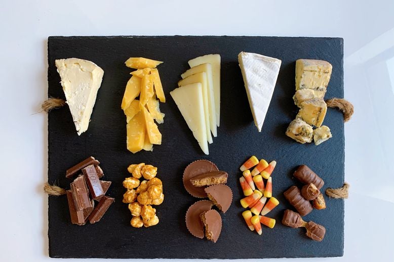 Pairs of blue cheese and Twix, brie and candy corn, manchego and Reese's, Gouda and caramel popcorn, and triple-cream cheese and Kit Kats, arranged on a serving board