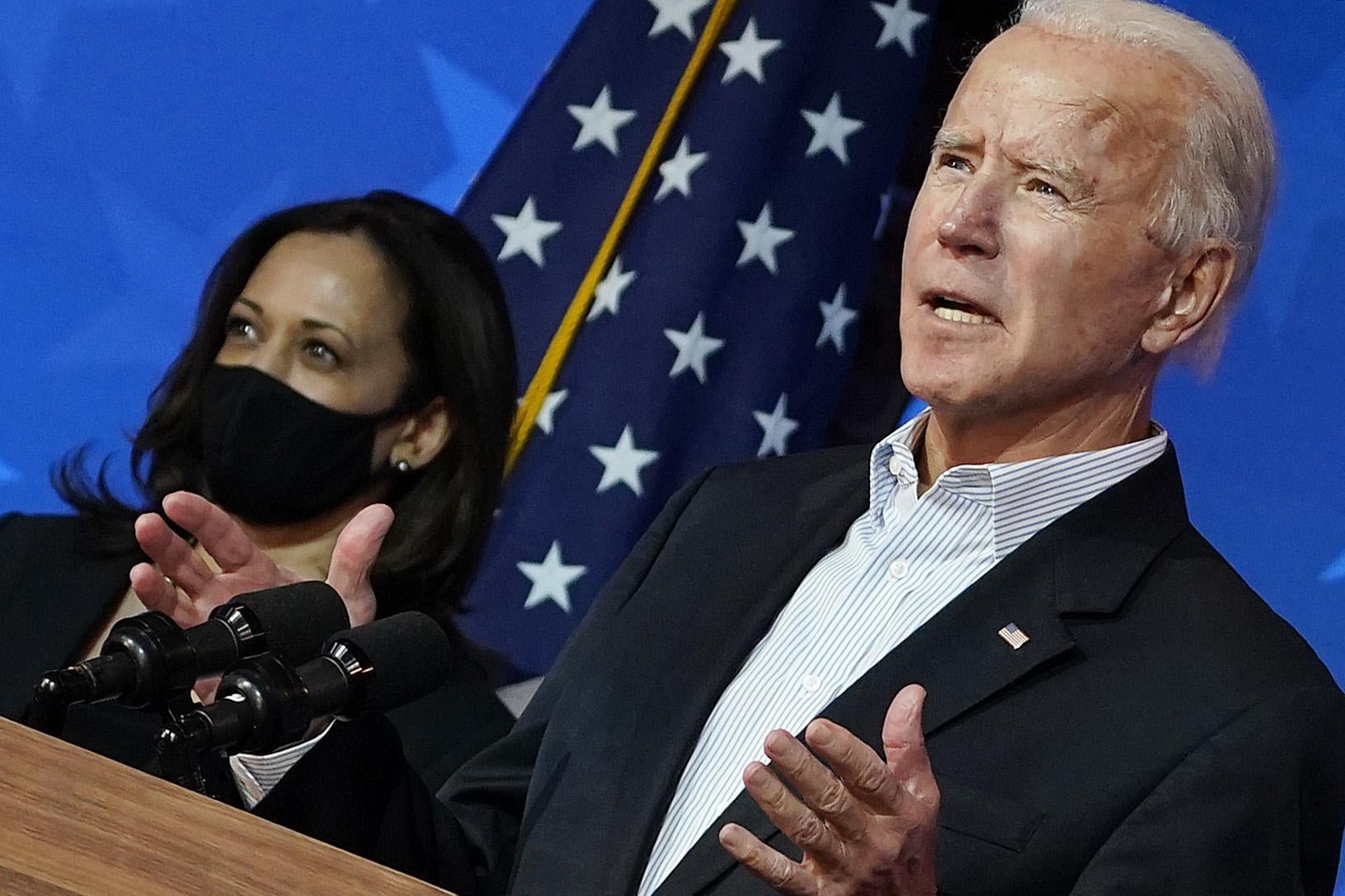 Biden speaks with a masked Harris and a flag behind him. 
