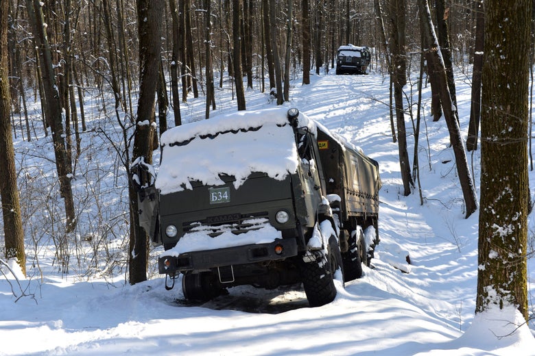 Two military trucks in the woods covered in snow.