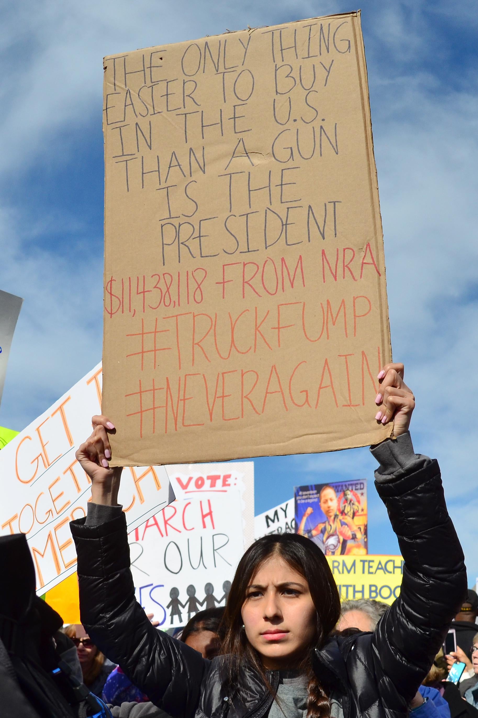 A woman hoists a poster reading, "The only thing easier to buy in the U.S. than a gun is the president."