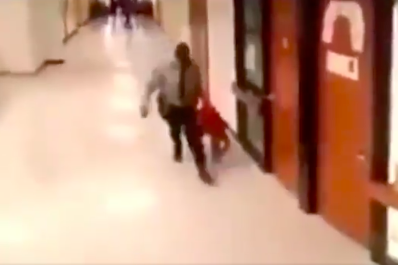 A screengrab of the surveillance video. The deputy is seen holding up a student dressed in red as he walks down the hallway. 