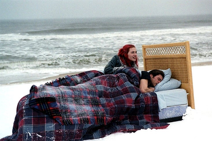 Kate Winslet and Jim Carrey recline in a bed on a snowy beach.