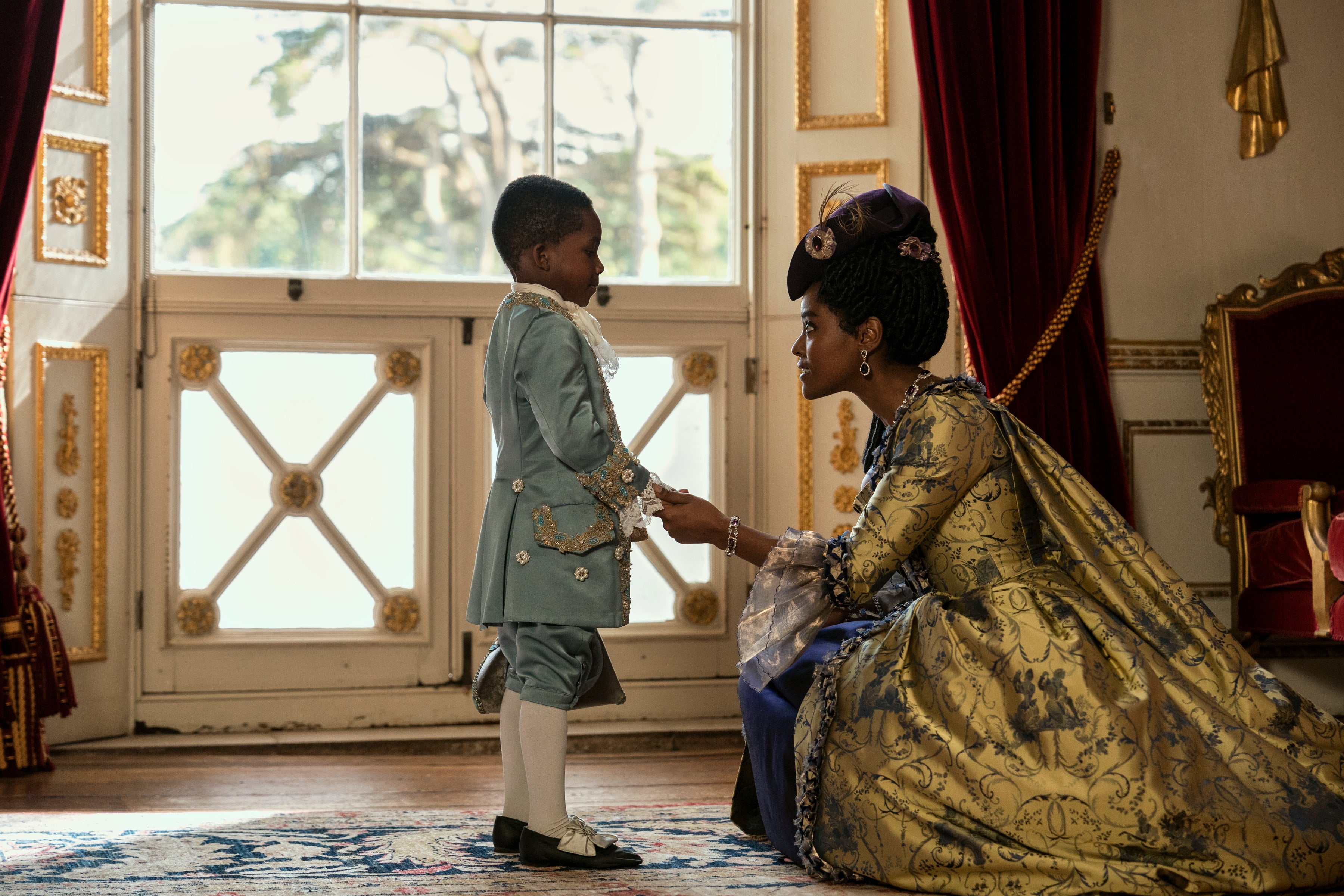 A woman in a gorgeous dress kneels to speak to a boy about five years old.