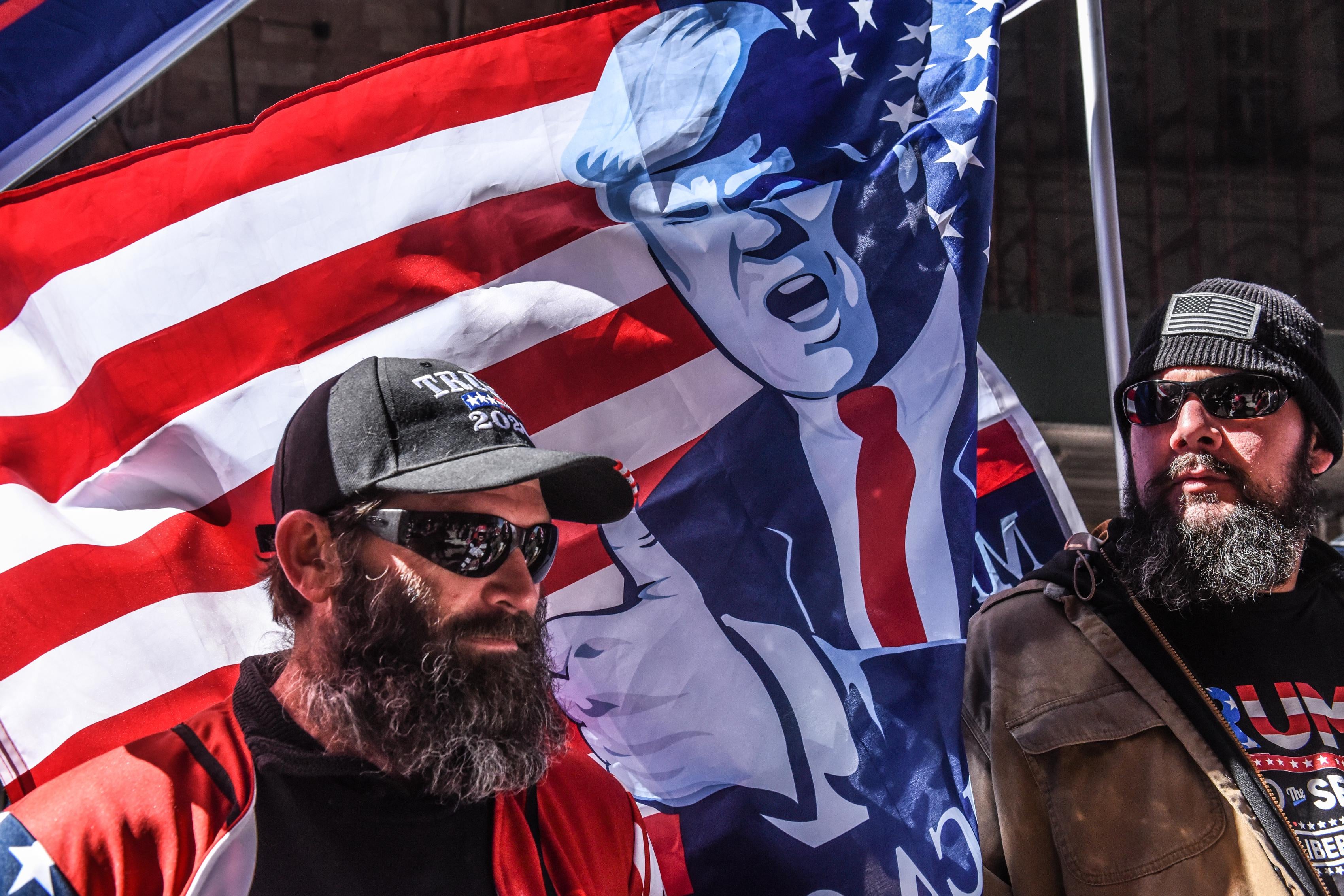 Two men in front of an American flag with Trump on it.