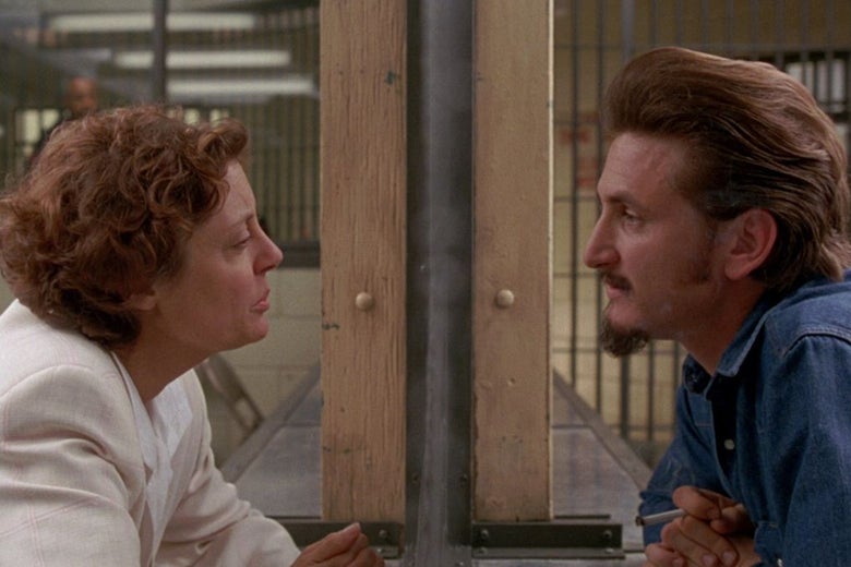 The profile of Susan Sarandon faces right looking at the left facing profile of Sean Penn behind a pane of glass as he's dressed as a prisoner. 