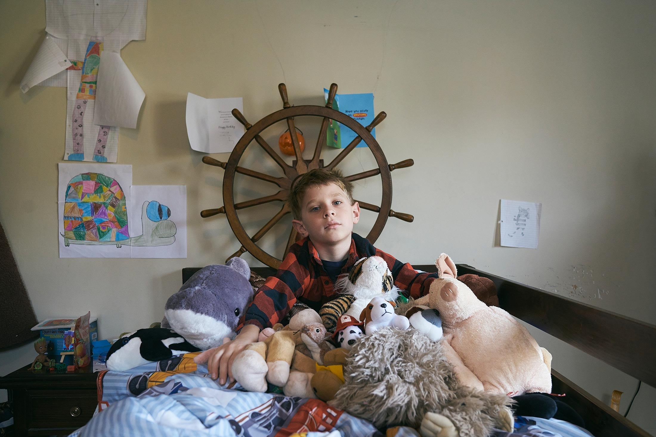 Colin, surrounded by his stuffed animals sitting on his bed.