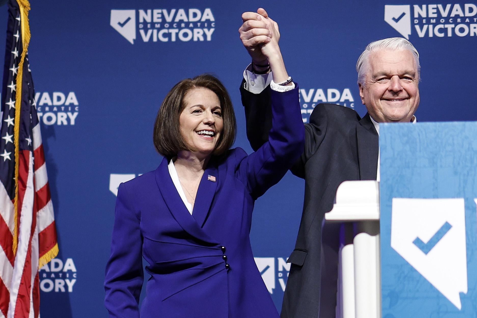 U.S. Sen. Catherine Cortez Masto (D-NV) and Nevada Gov. Steve Sisolak holding hands in the air in celebration.