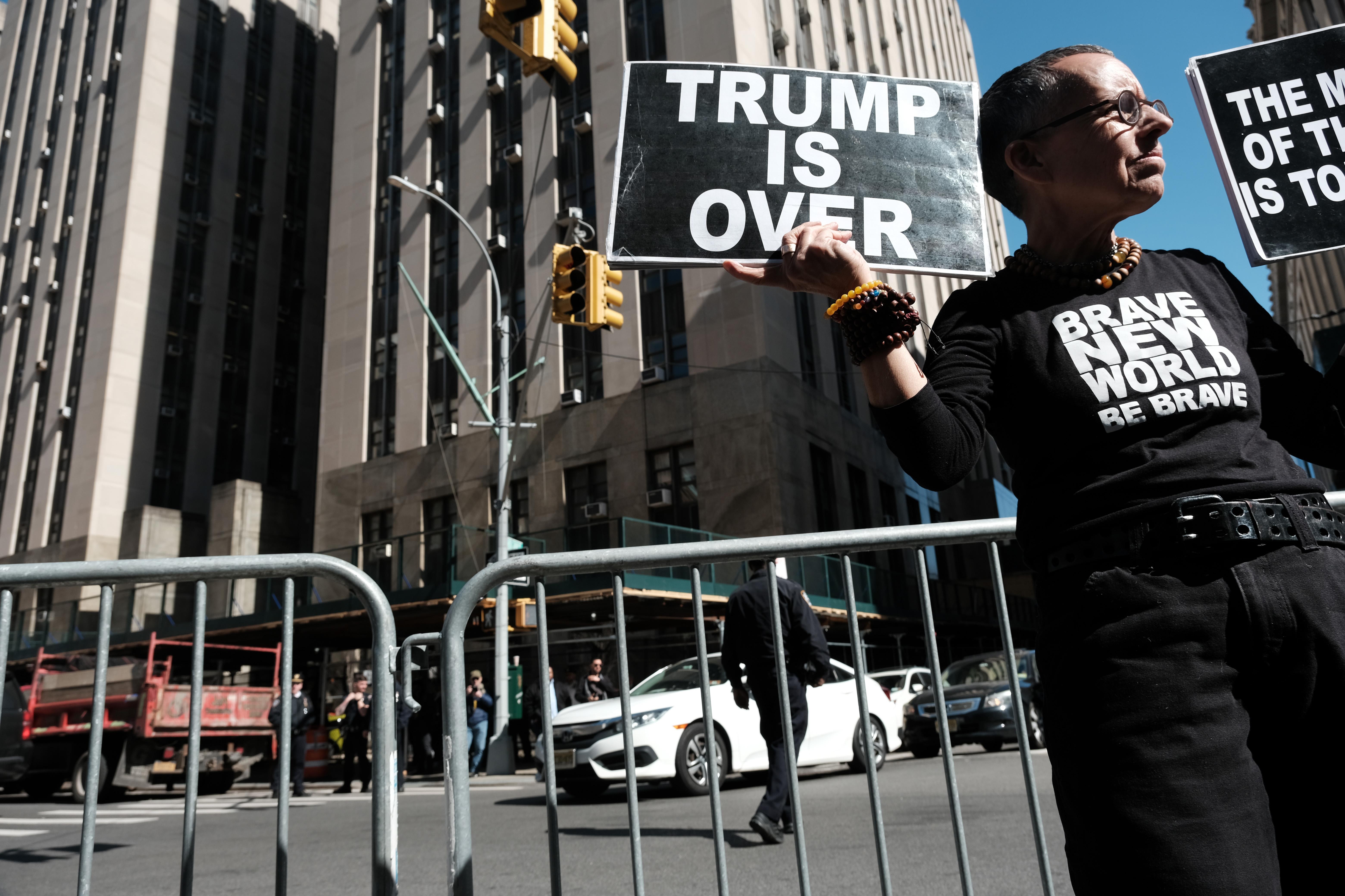 A person wearing all black holds up a sign that says, "TRUMP IS OVER" on a Manhattan street corner.