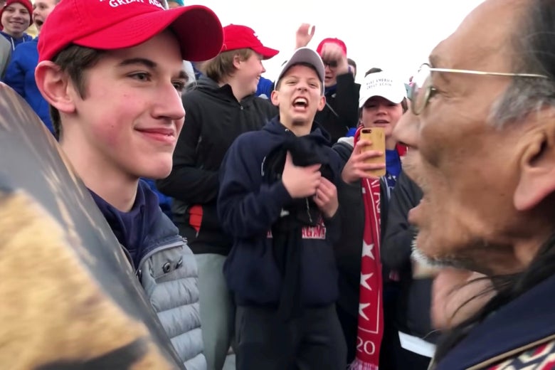 Nicholas Sandmann in a MAGA hat with teenagers around him as stands across from Nathan Phillips.