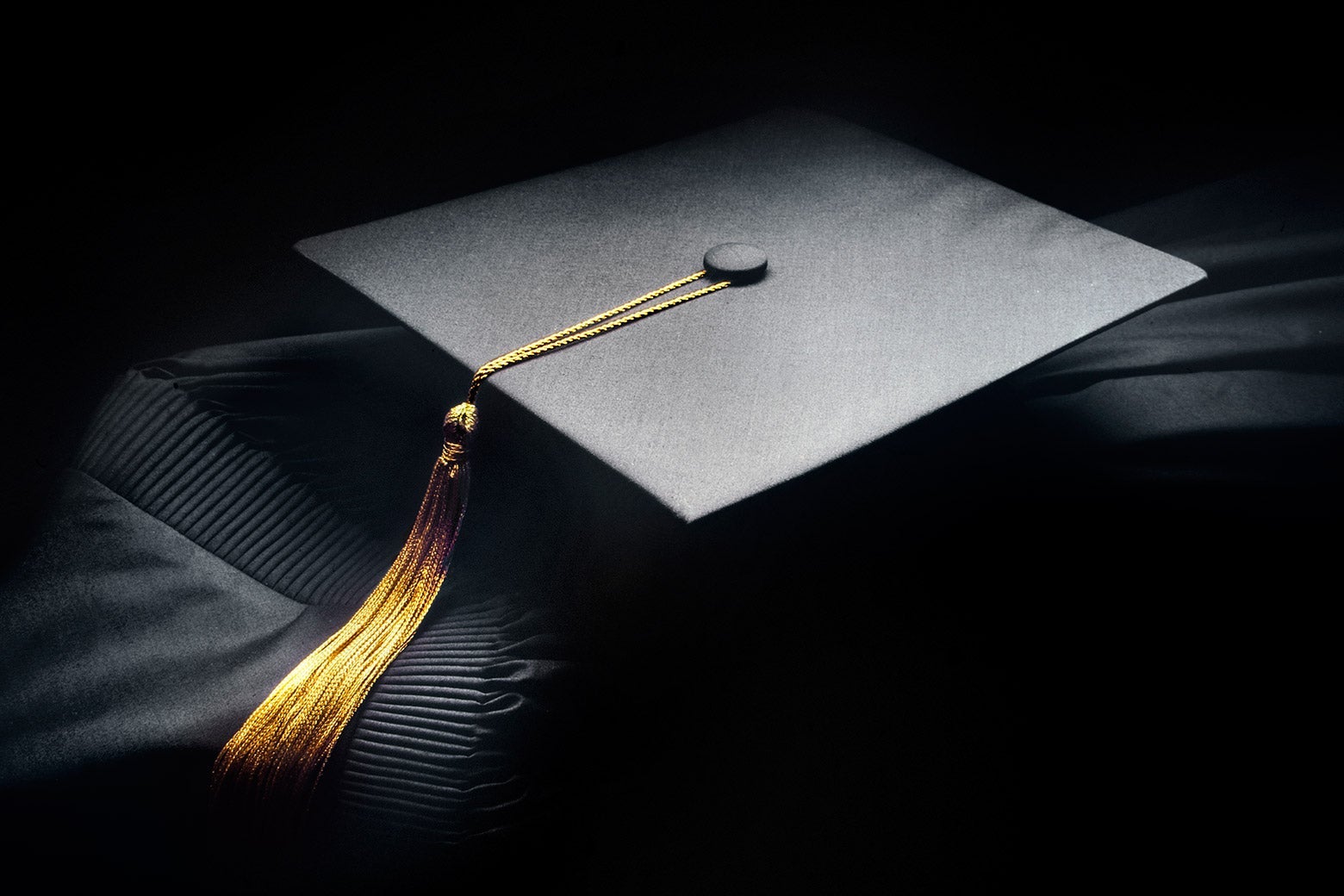 A graduation cap and a rolled up diploma in a dark room.
