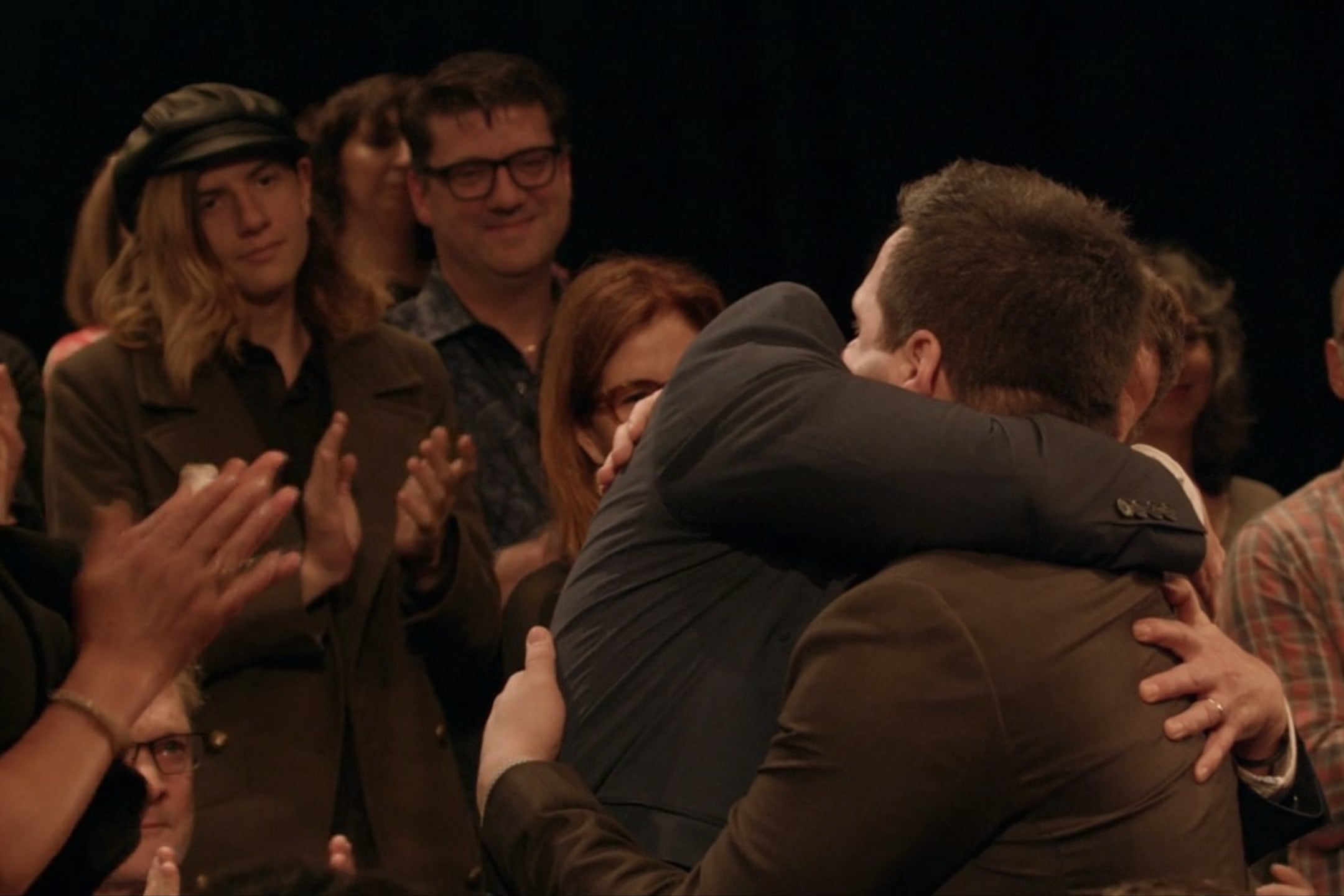 David Wain, stands and applauds as Derek DelGaudio embraces his mom.