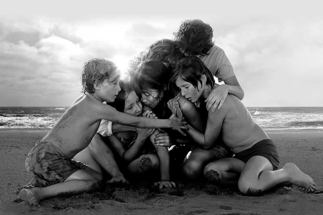 Children huddle around one another and a female adult on the beach.