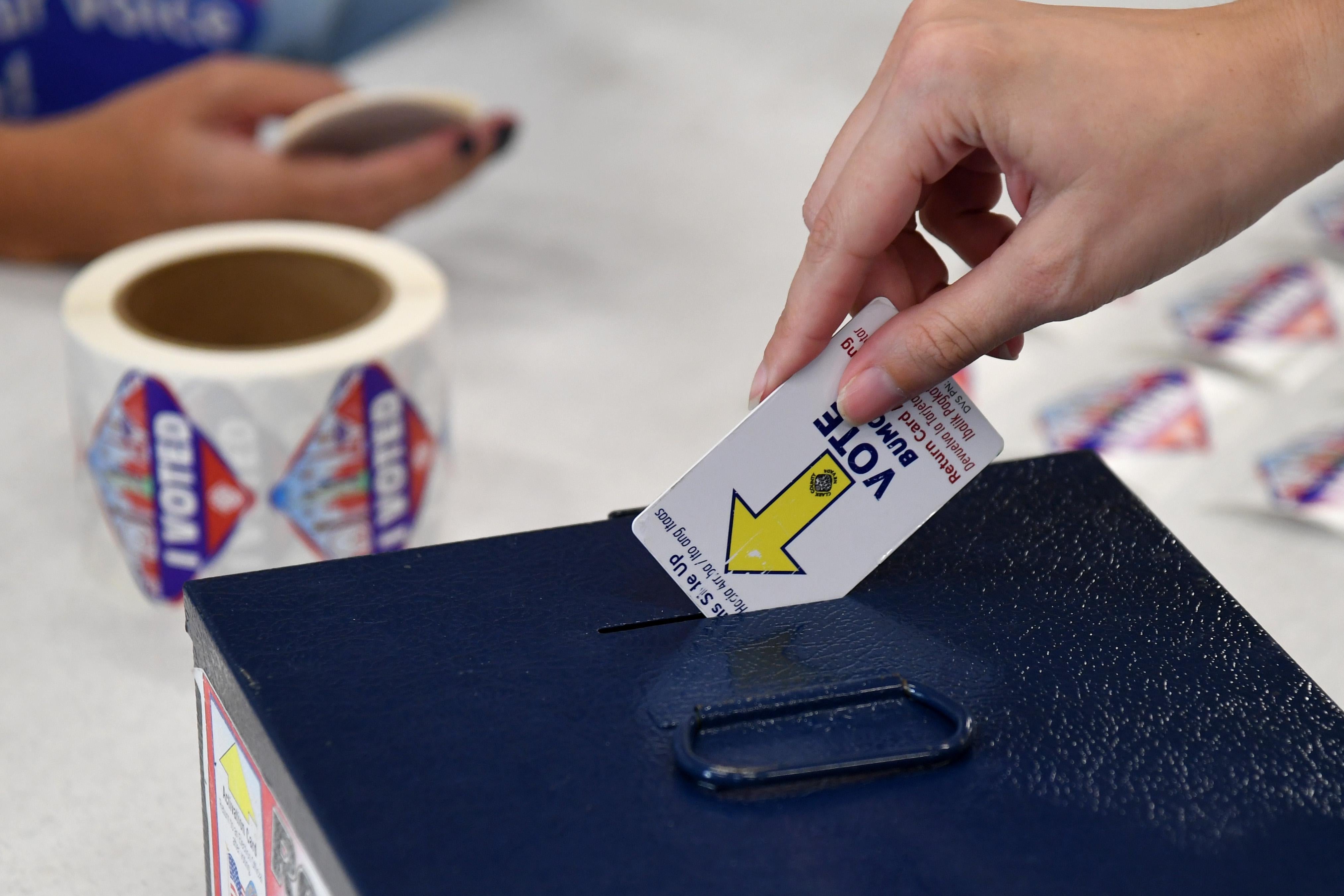 A hand drops a card in a ballot box.