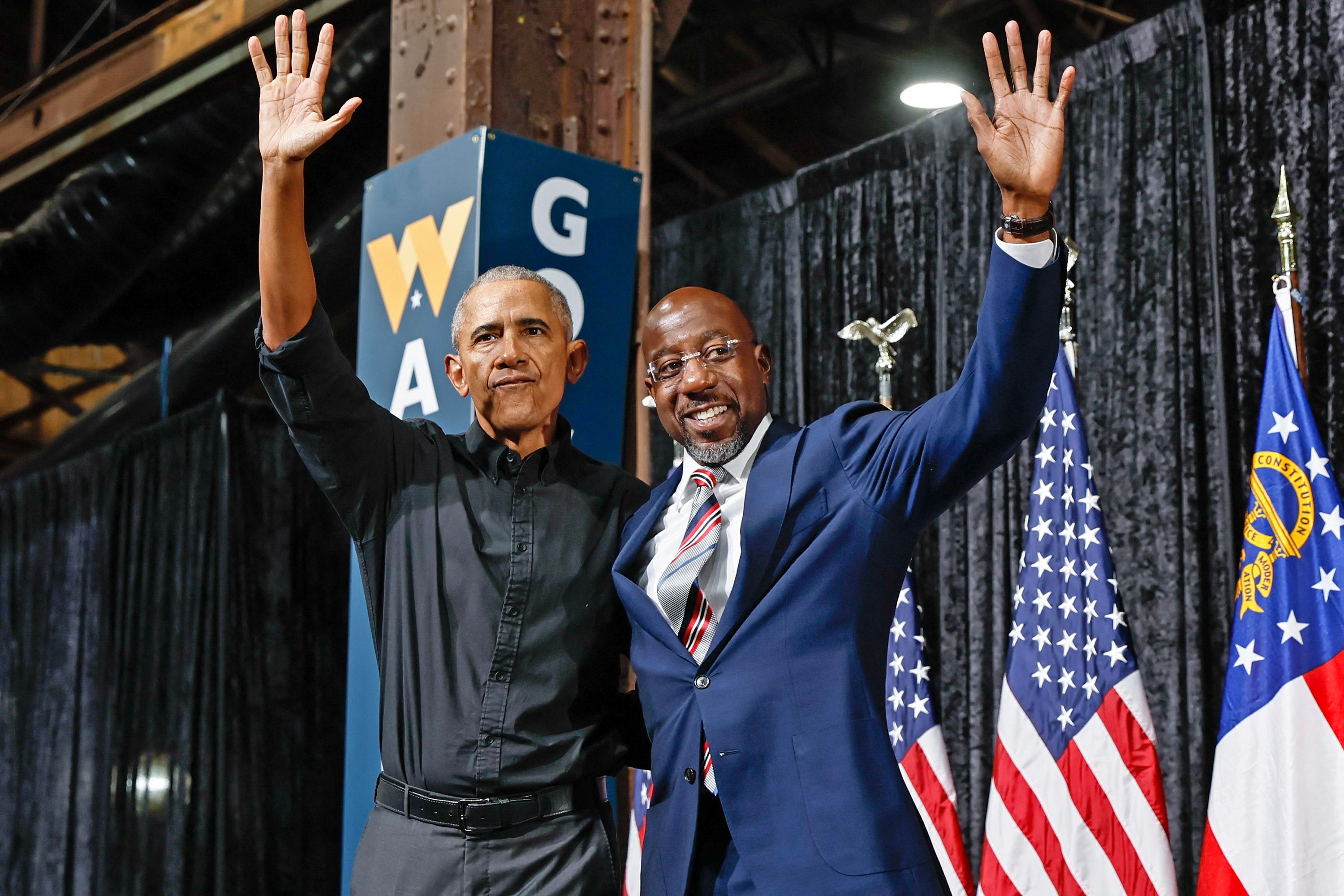Two men wave from a stage.