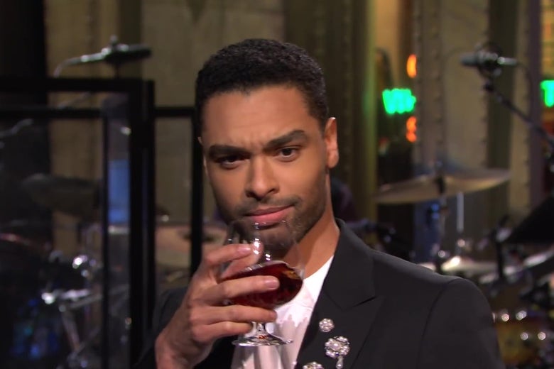 Regé-Jean Page, on the SNL stage, holding up a snifter of cognac, raising one eyebrow, and looking into the camera.