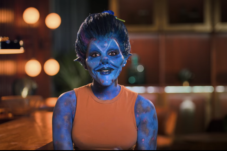 Woman in orange shirt dressed as a blue pixie.