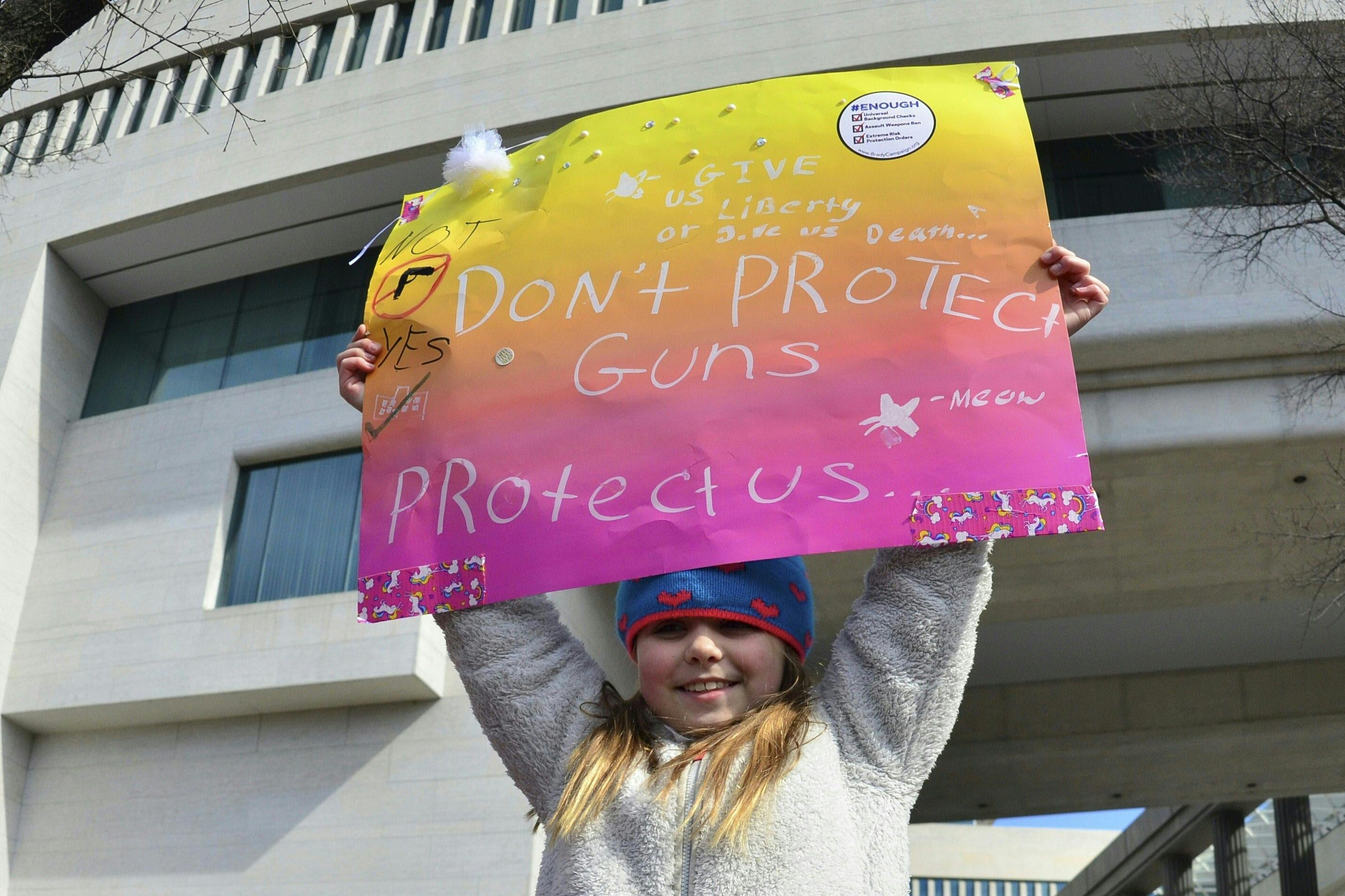 A little girl hoists a placard reading, "Don't protect guns protect us."