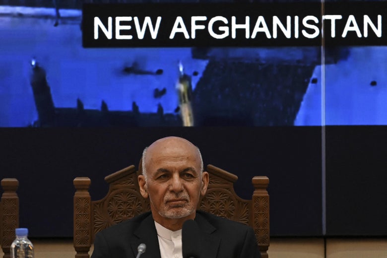 Ghani sits in a chair in front of a screen that has the words "New Afghanistan" on it