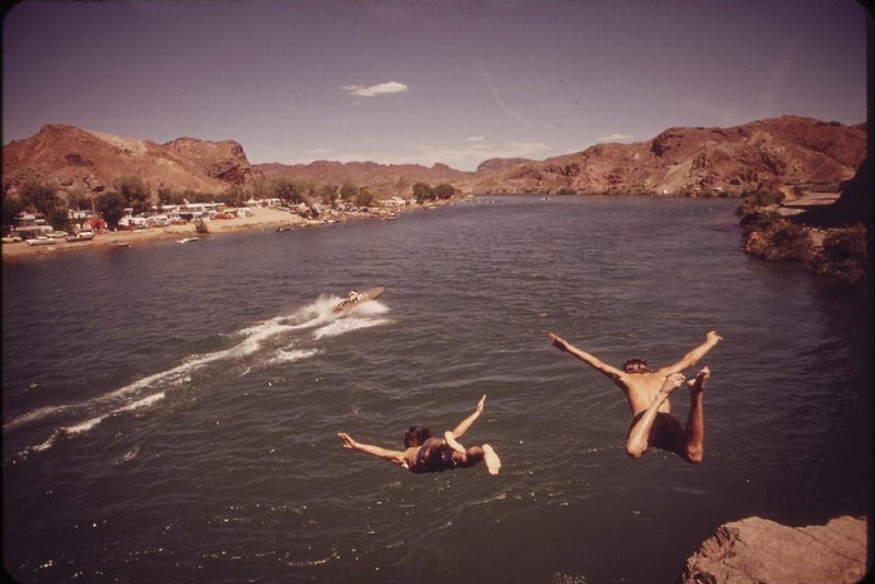 Two teenagers leap from a cliff into a river.
