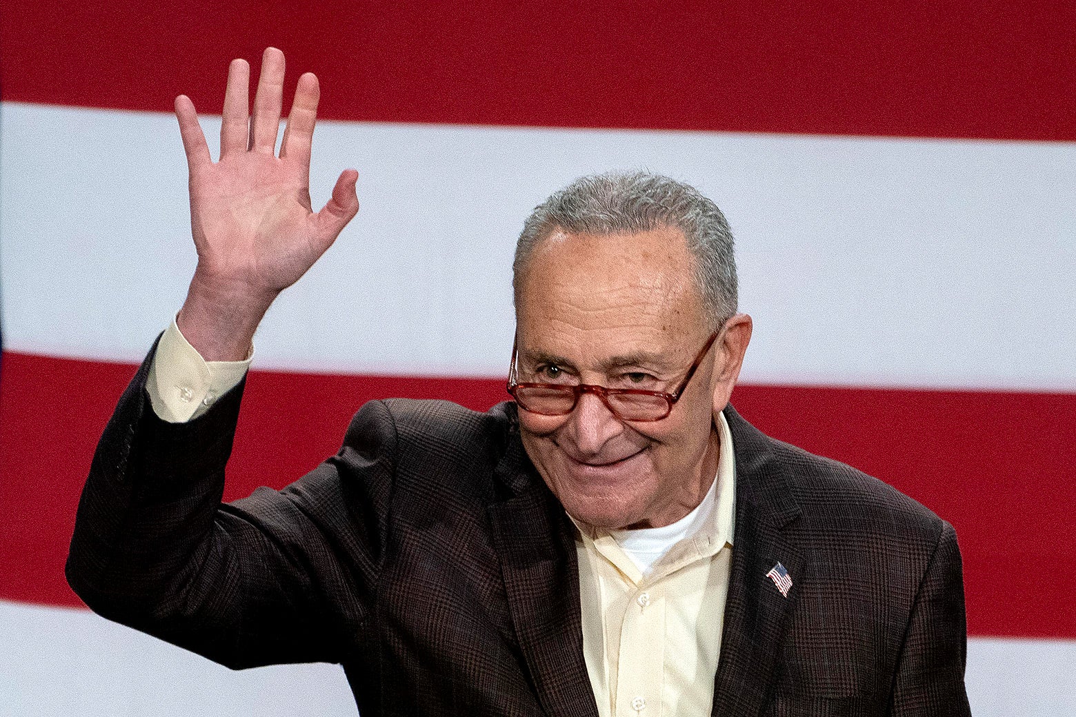 Chuck Schumer waving in front of an American flag.