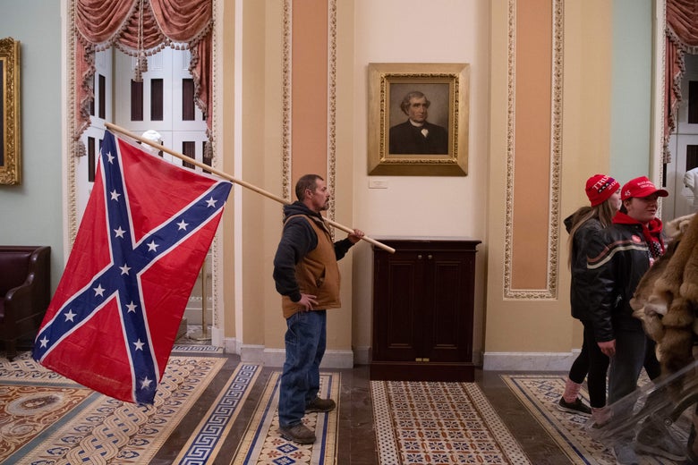 A Trump supporter carrying a Confederate flag stands in front of a painting in the hallway of the Senate chamber on Jan. 6.