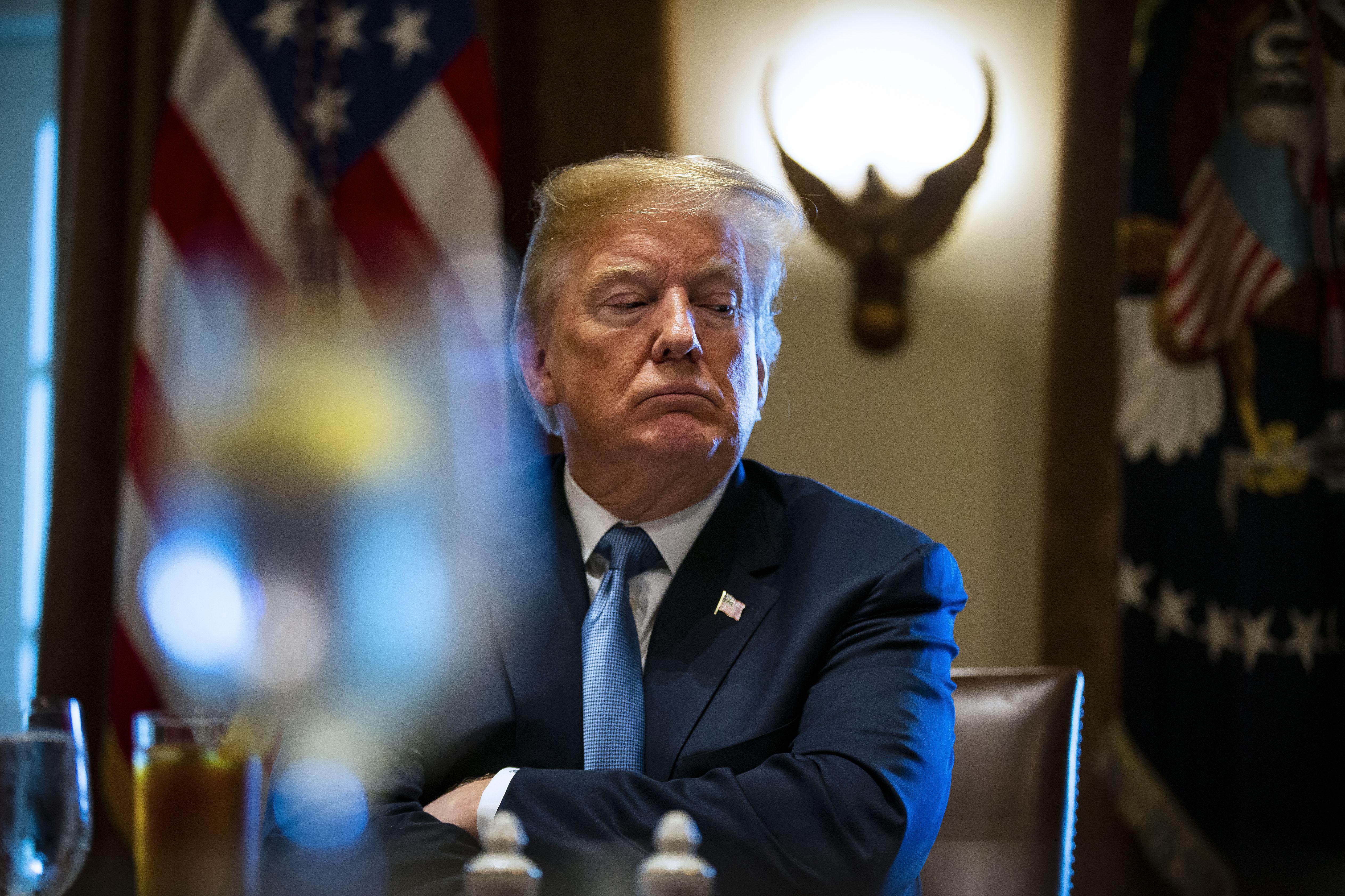 President Trump, seated at a table, crosses his arms and looks downward.