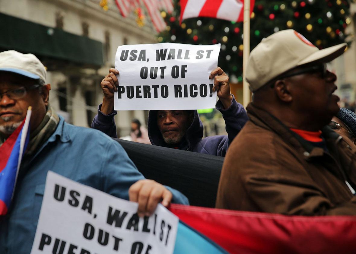 People protest outside of Wall Street against cutbacks and austerity measures forced onto the severely indebted island of Puerto Rico on December 2, 2015 in New York City. 