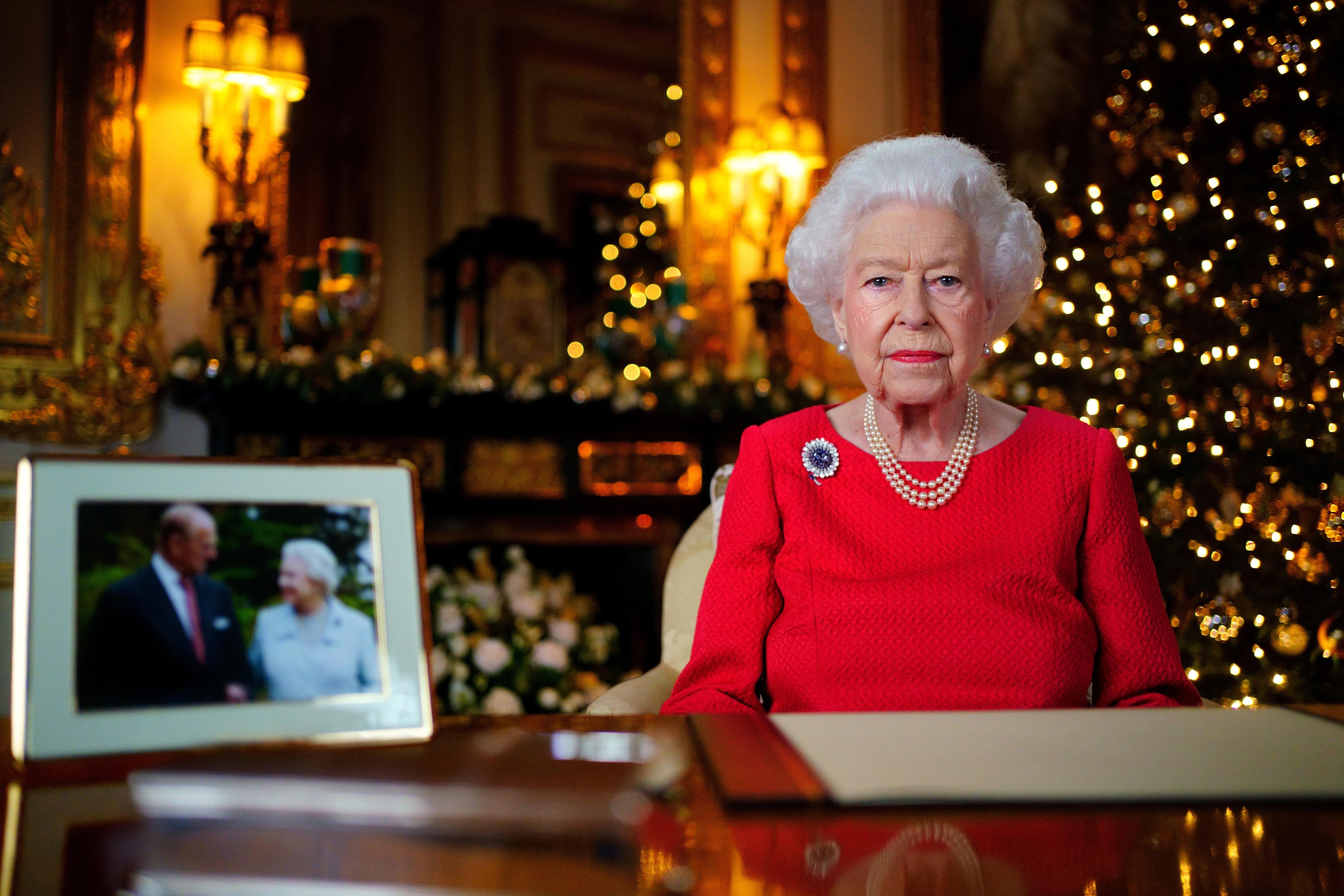 Queen Elizabeth II sits behind a wooden desk that holds a framed photograph of the queen and her late husband