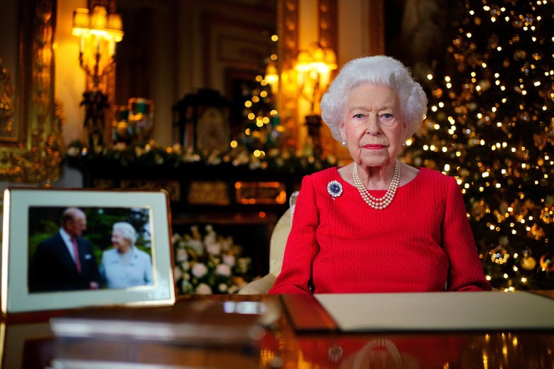 Queen Elizabeth II sits behind a wooden desk that holds a framed photograph of the queen and her late husband