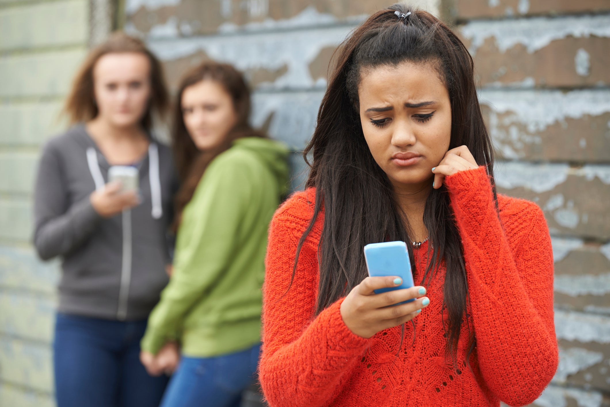 A teen girl looking sad at her phone because of cyberbullying.