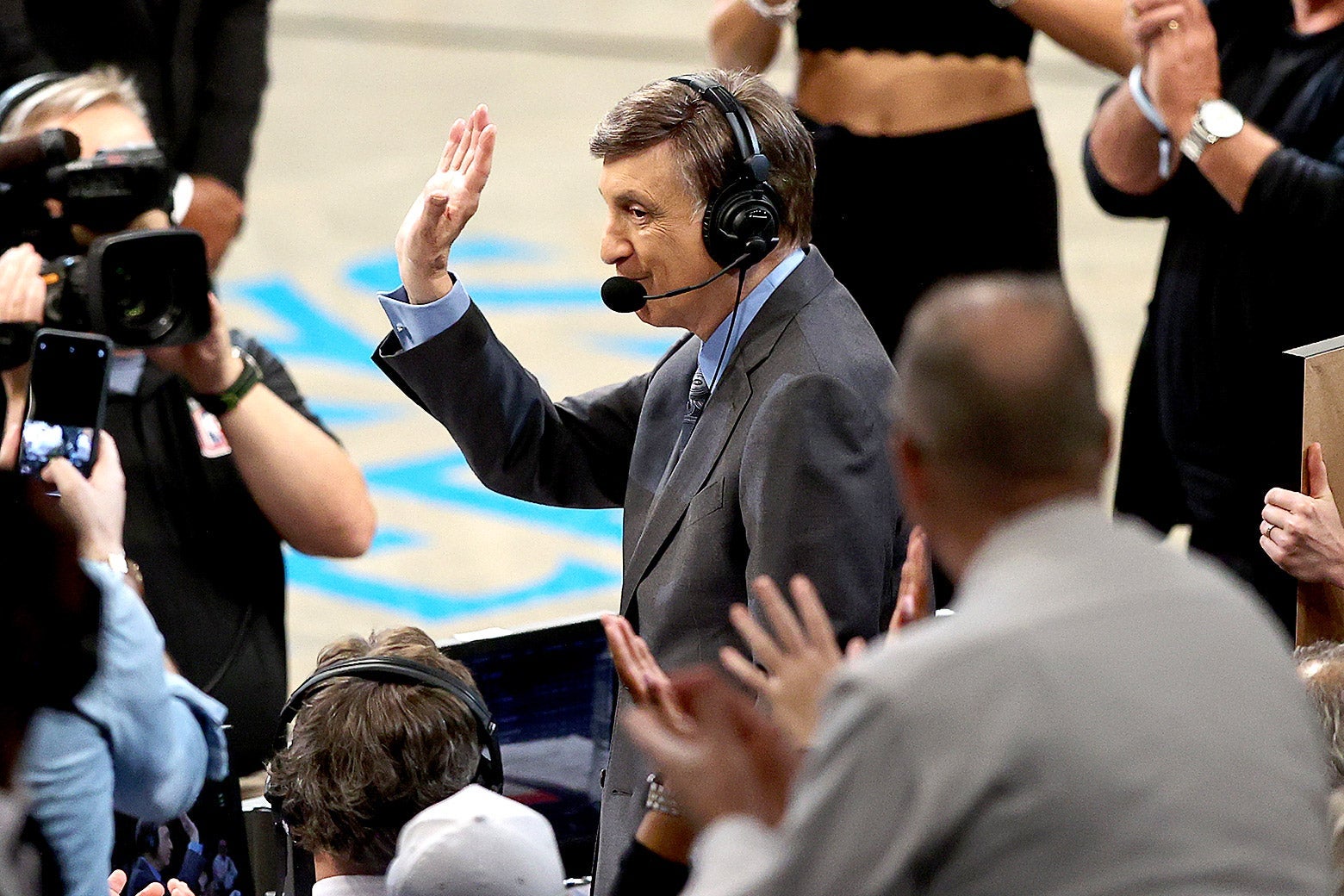 Marv Albert standing with headset on courtside, as the crowd cheers