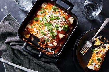 A pan full of enchilada, sprinkled with green garnish.