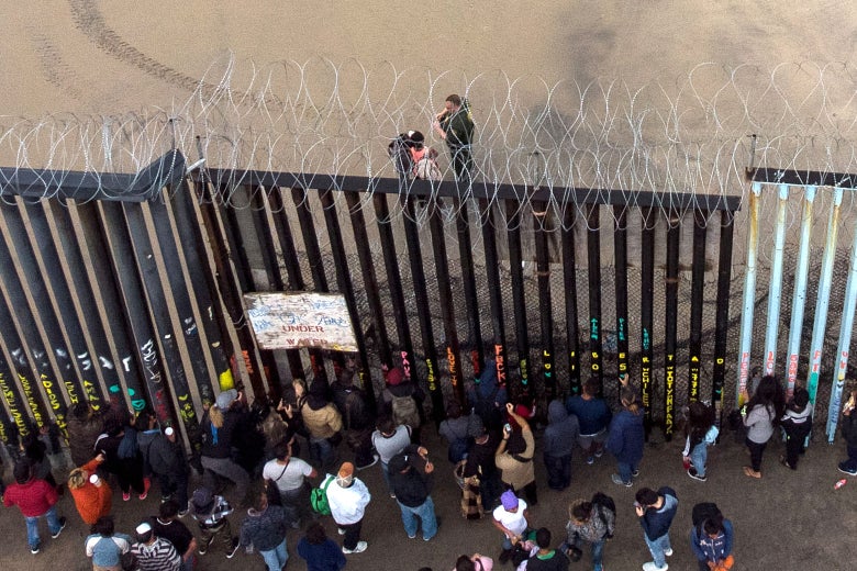Aerial view of migrants standing at the border fence.