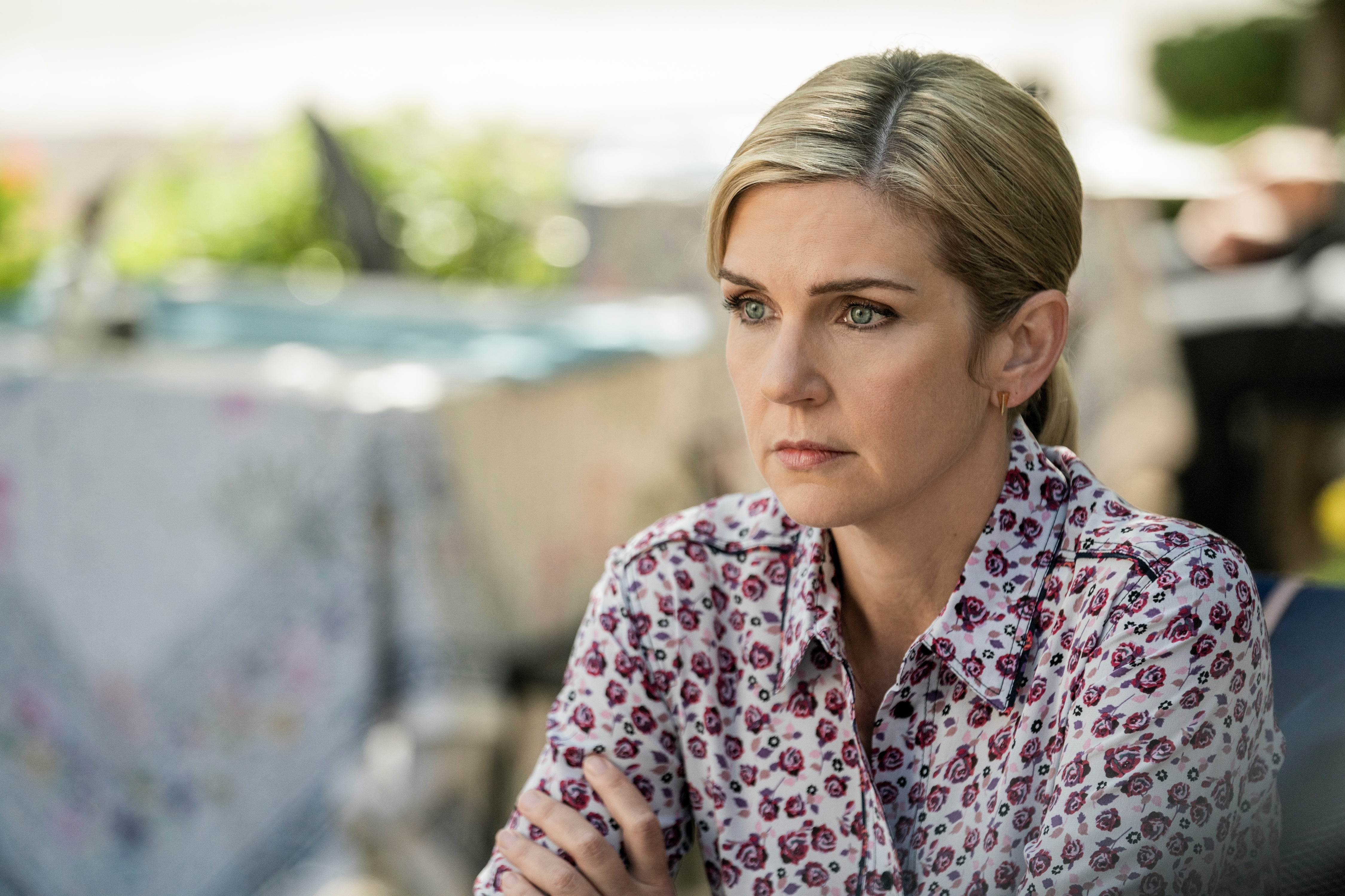 A blond woman in a print shirt stares off into the distance.