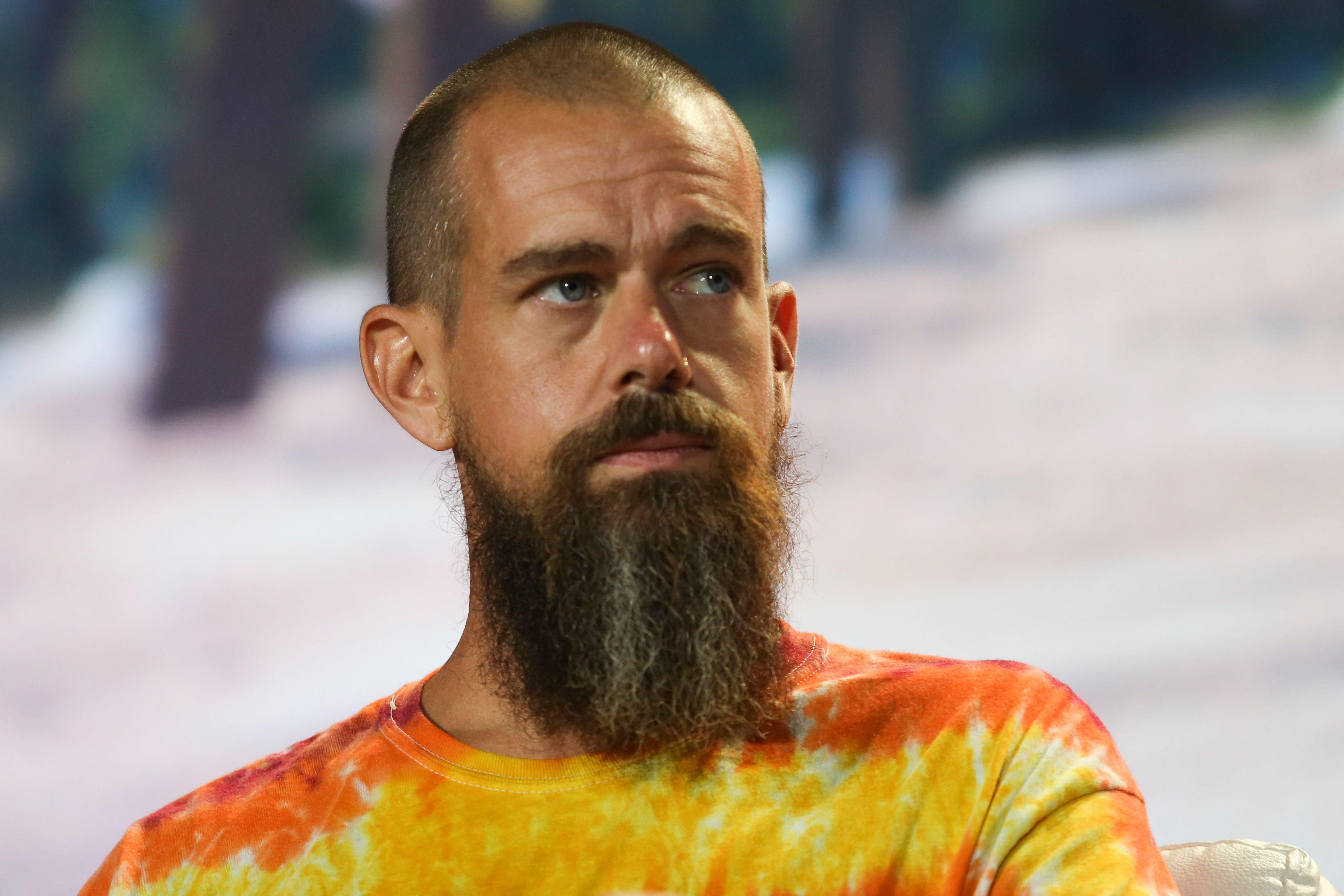 Jack Dorsey wears a tie-dye T-shirt on stage in front of a tropical background.
