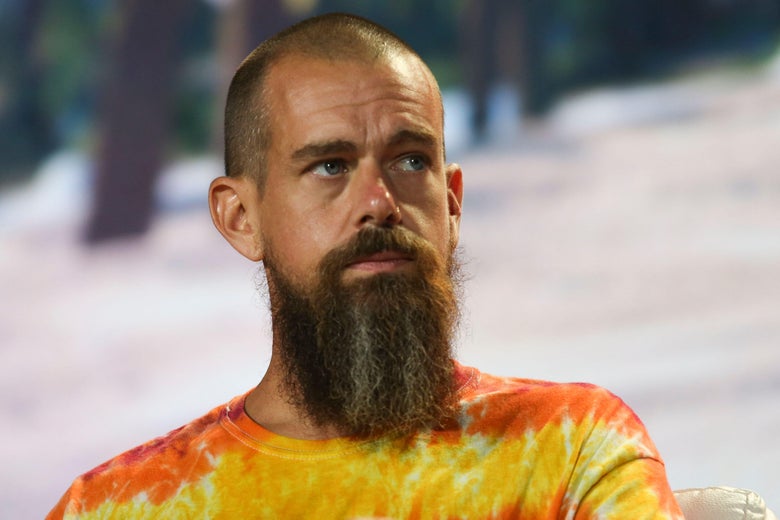 Jack Dorsey wears a tie-dye T-shirt on stage in front of a tropical background.